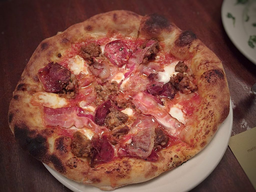 Pizza topped with meat, tomato and mozzarella on a plate at Pizzeria Mozza in Los Angeles.