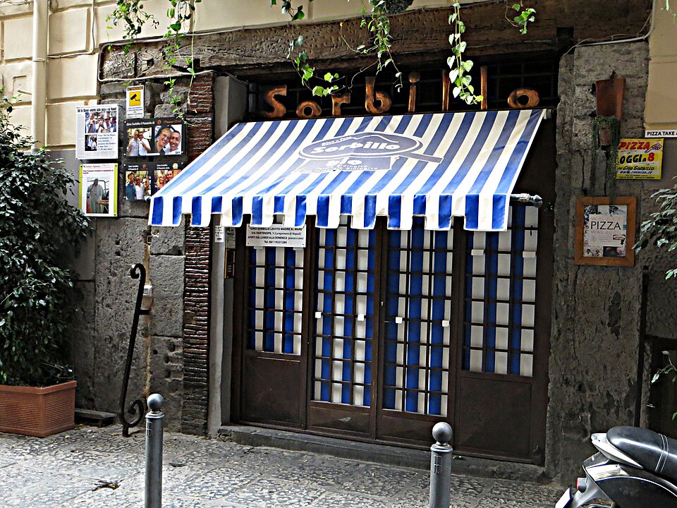Gino Sorbillo’s entrance with a blue-and-white striped awning on Via dei Tribunali in Naples, photographed in 2015.